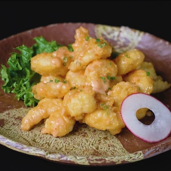 Crispy fried shrimp coated in a creamy orange sauce, garnished with lettuce and a radish slice.
