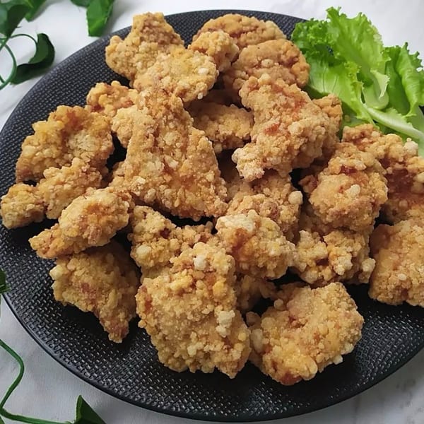 Crispy fried chicken bites on a black plate, garnished with fresh green lettuce.